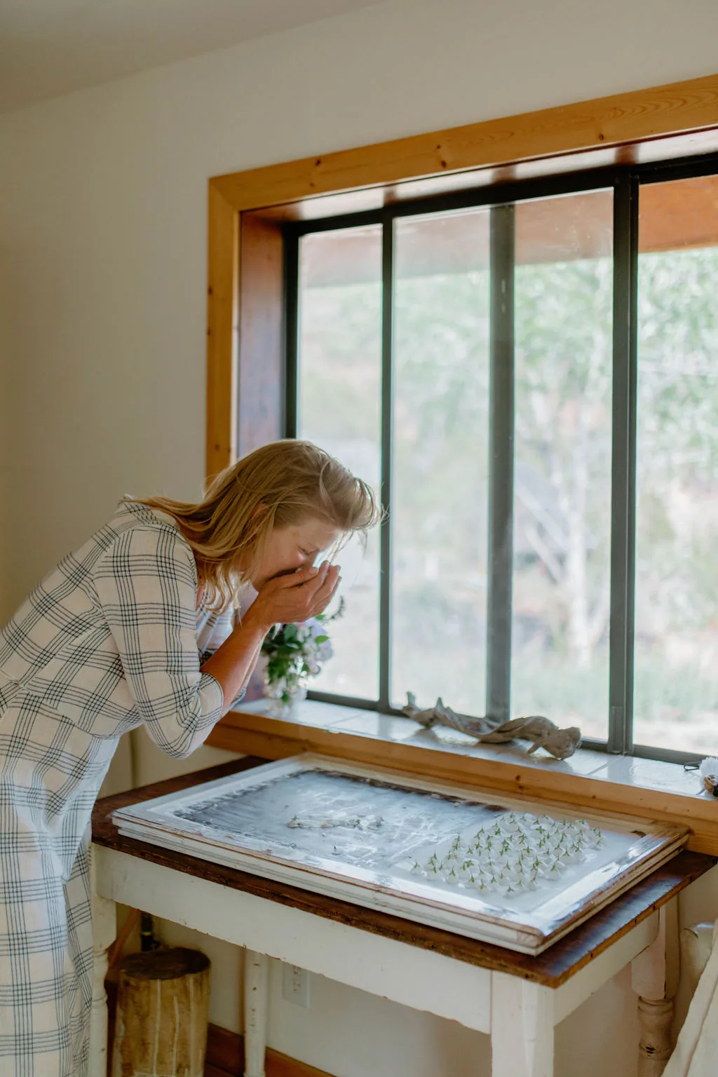 Kate leaning over the enfleurage tray at a bright window