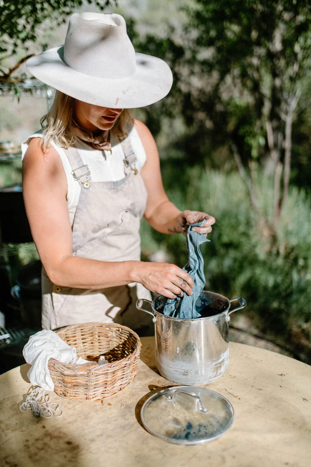 Kate lifting woad-dyed cloth from a steel dye pot outdoors