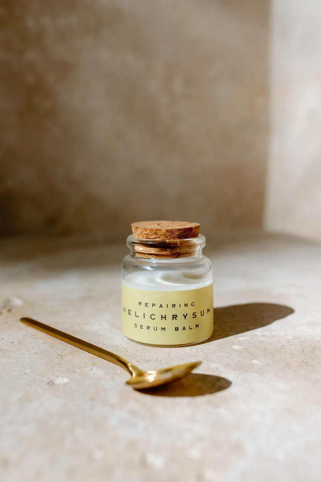 Repairing Helichrysum serum balm in a corked jar, a gold spoon beside it