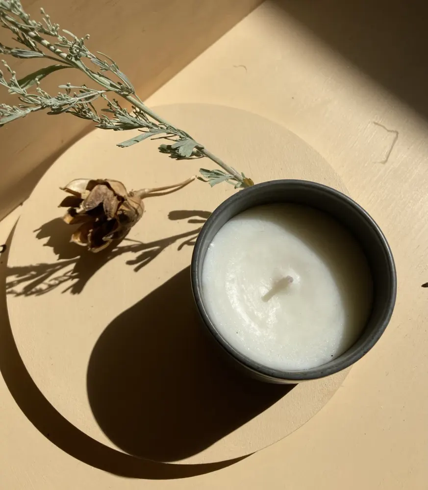A hand-poured tallow candle on a dish with a sprig of sage